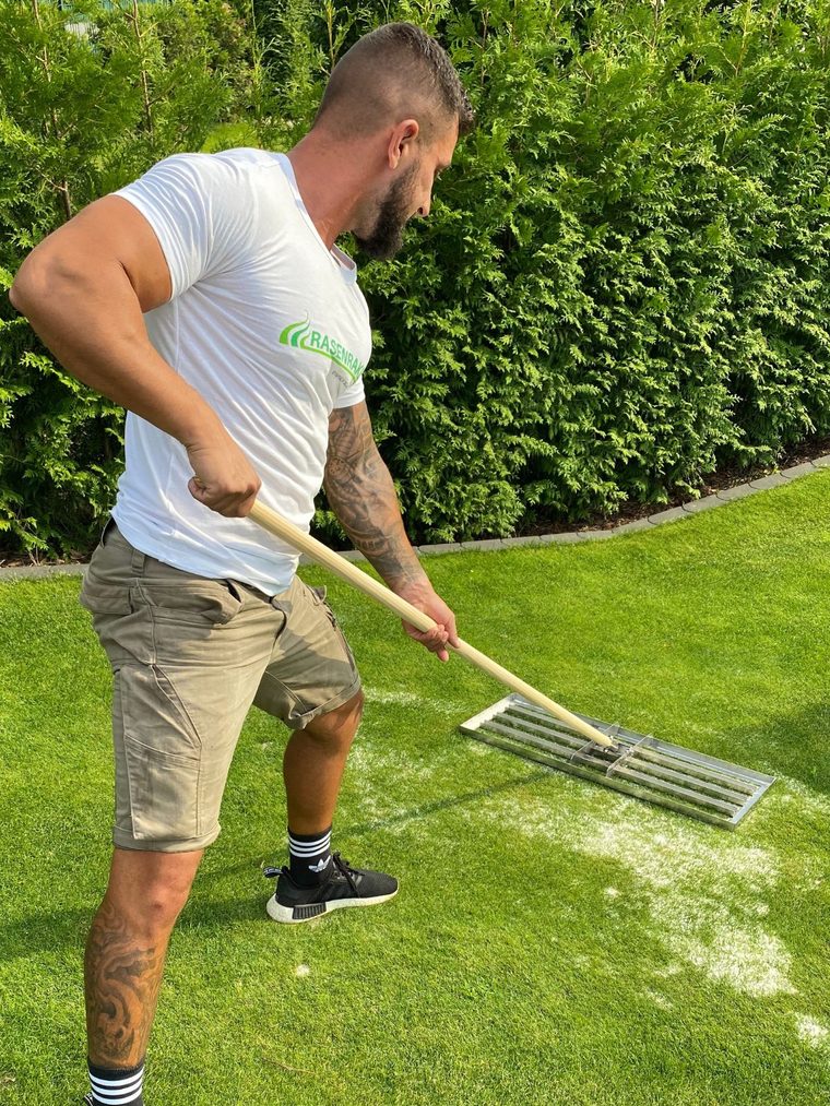 Ein Mann verteilt mit dem RISISANI Rasenrakel Sand auf einer Rasenfläche.